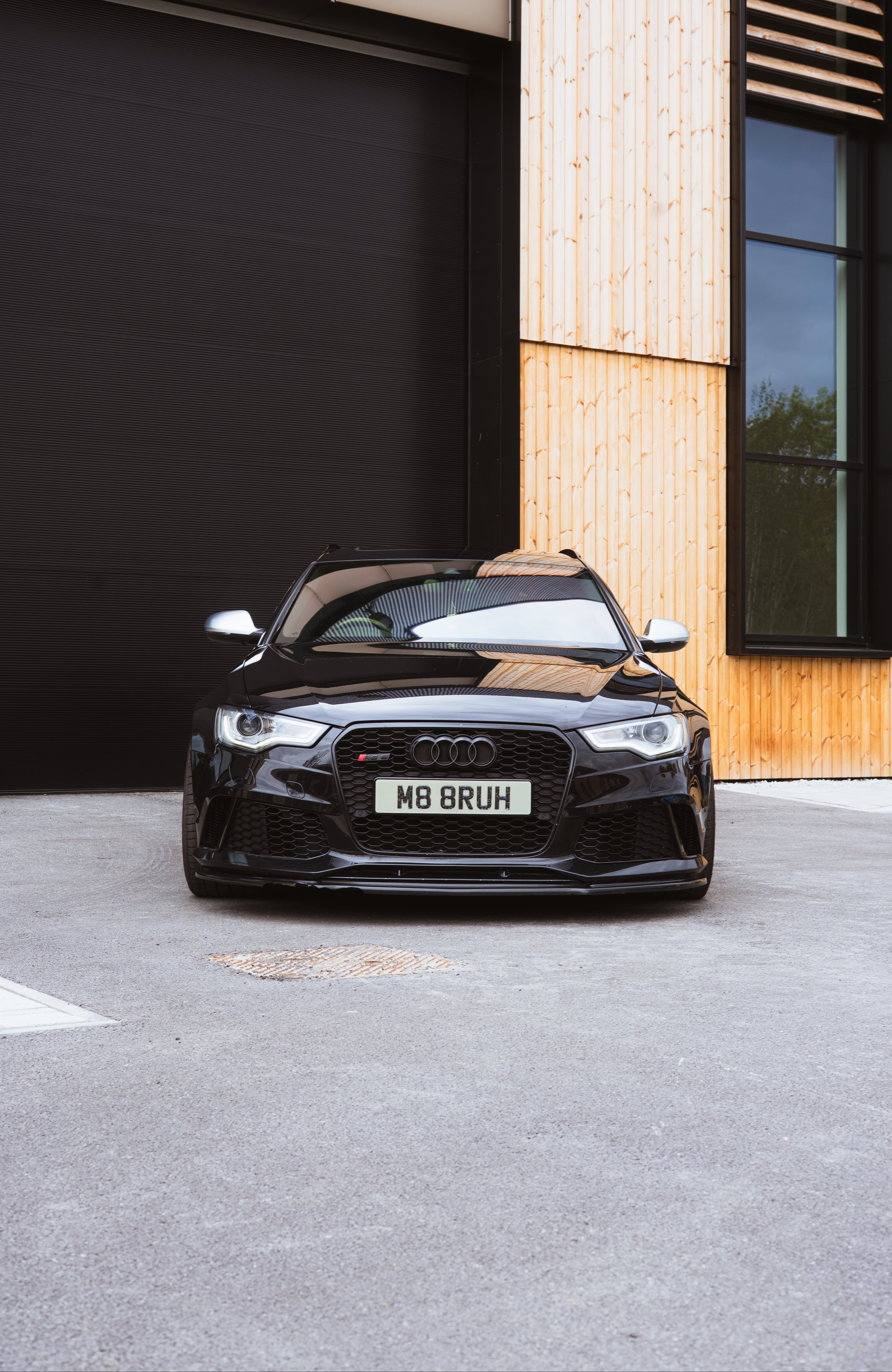 Black Audi car with a personalized license plate in front of a modern building.